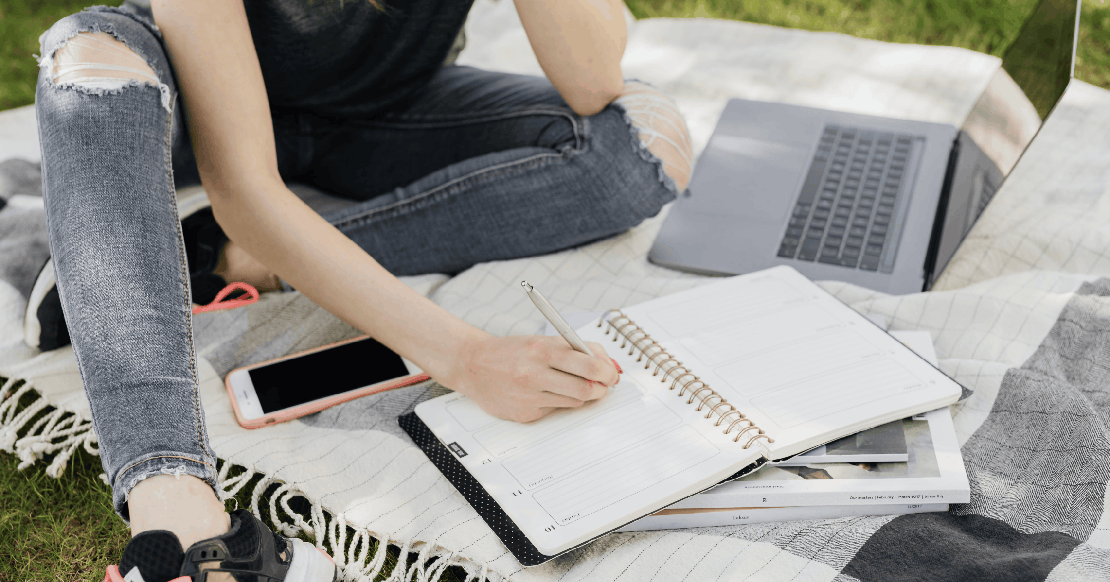 Student sitting in the grass writing with laptop and journal